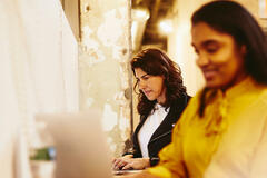 two females working and smiling on their laptops in an office