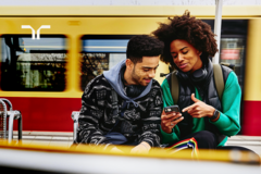 two persons at train station looking at smartphone