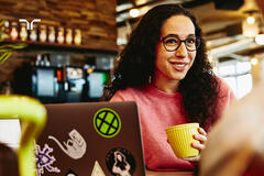 woman at cafe with laptop and holding coffee cup