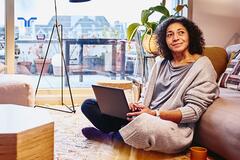 smiling woman sitting on living room floor with laptop and coffee mug