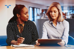 woman with notepad speaking to woman with tablet