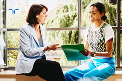 woman holding a coffee mug conversing with a woman holding a folder