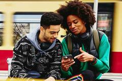 two friends looking at a phone at a train station