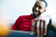 Smiling male sitting down, holding a ipad or laptop