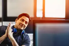Smiling male with headphones having a conversation at his desk. 

