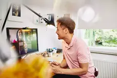 male sitting at desk in his home office, meeting colleagues in a online meeting.

