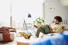 male sitting down on a couch writing in a notebook. focused.
