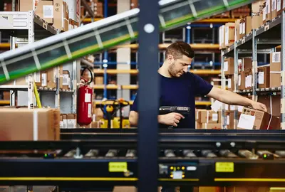 male scanning a package, standing behind a conveyor belt.
