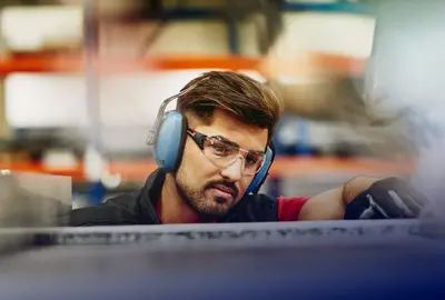 male wearing protective ear covers, safety gloves and safety glasses on a production site