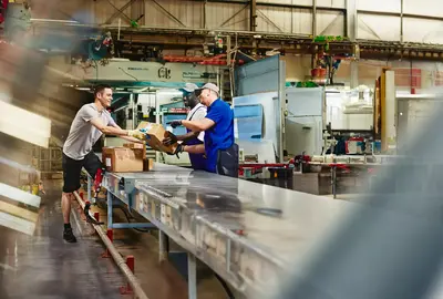 Three people working next to an assembly line with packages. 

