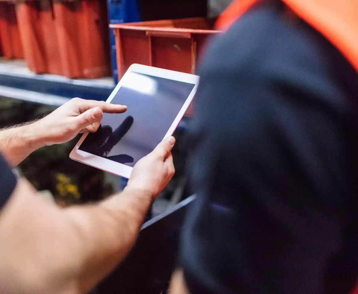 Close up of two workers using tablet computer at factory warehouse. Foremen with colleague using digital tablet in warehouse.