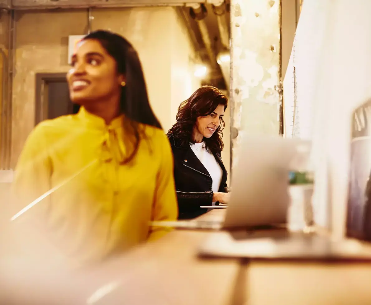 Two smiling female working on their laptop.
