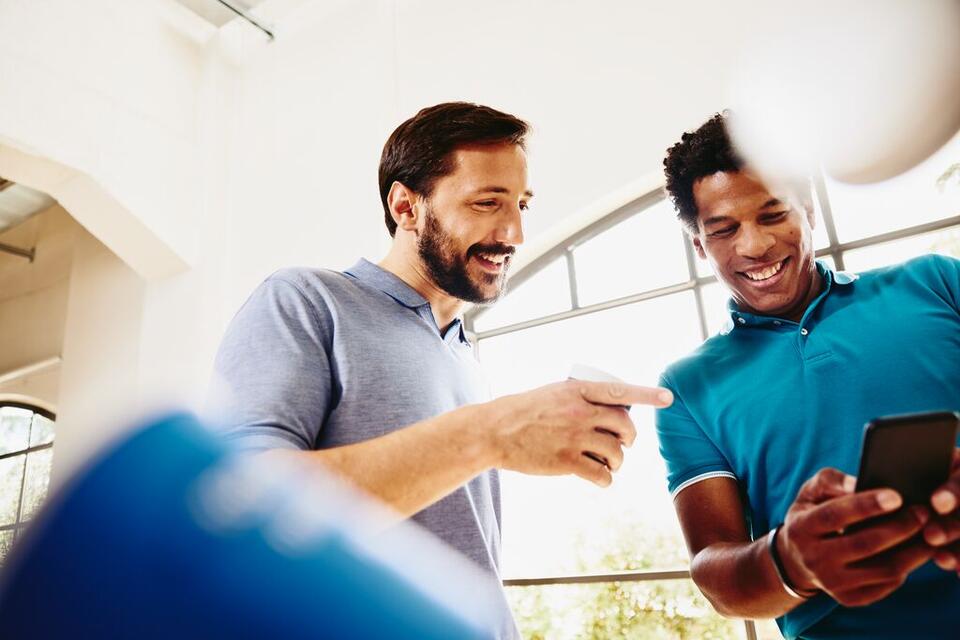 Two smiling colleagues (men) looking at a phone.