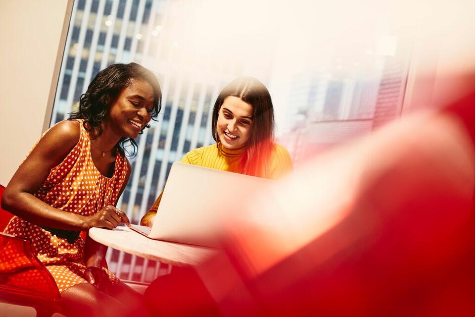 two females working and smiling on their laptops in an office